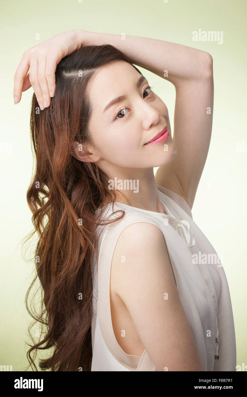 Femme coréenne avec la longue chevelure ondulée en blanc T-shirt mettant sa main sur sa tête et l'avant Banque D'Images