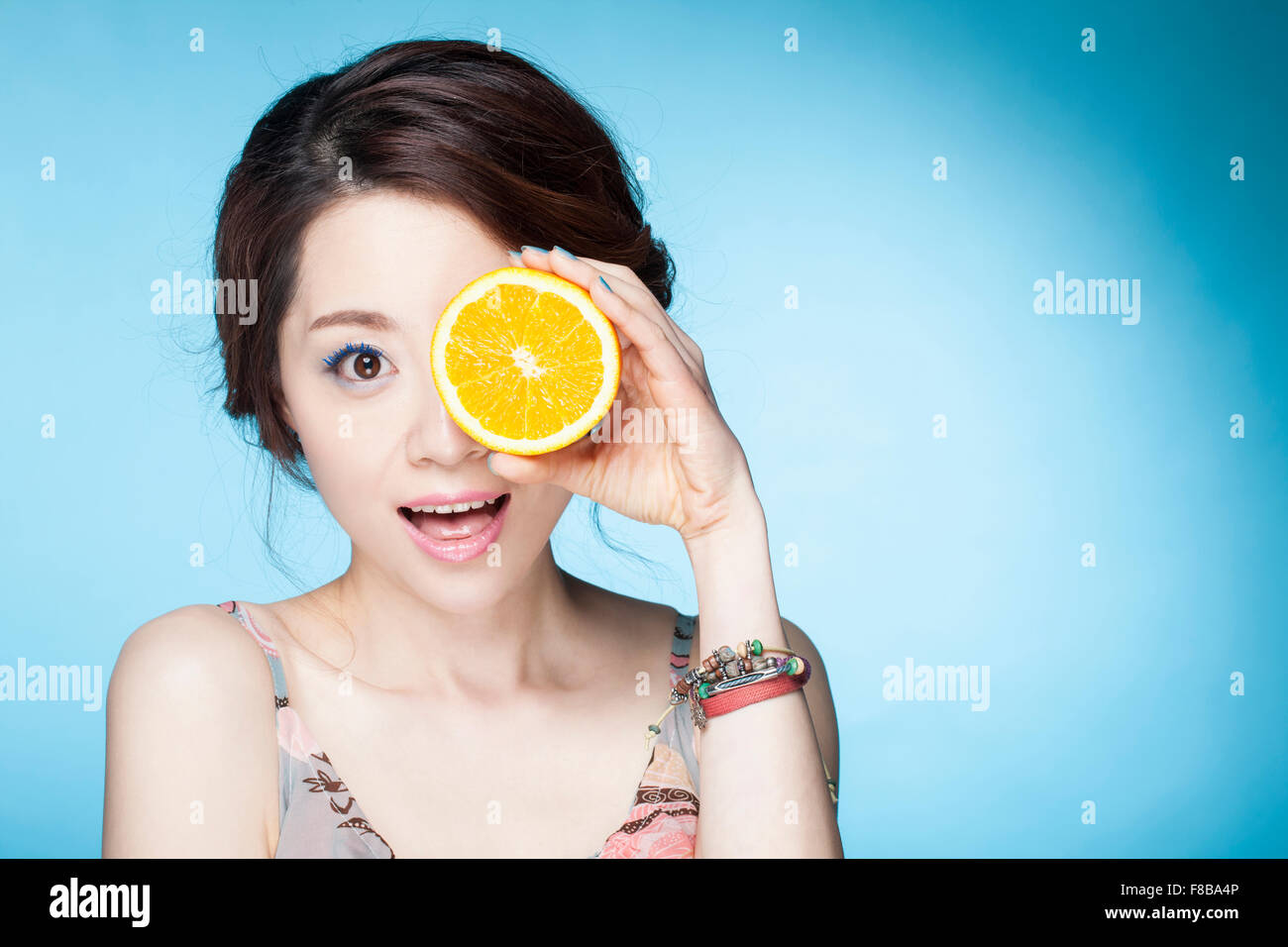 Femme surpris un œil avec une tranche d'orange avec un sourire Banque D'Images