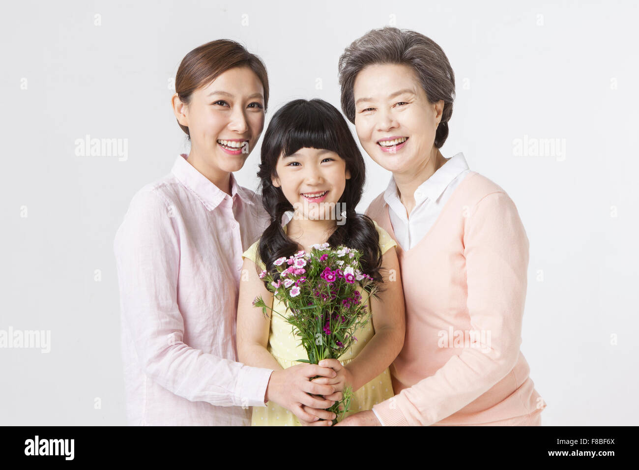 Fleurs tenus par des jeunes filles, les jeunes femmes adultes et senior woman tous les yeux de l'avant avec un sourire Banque D'Images