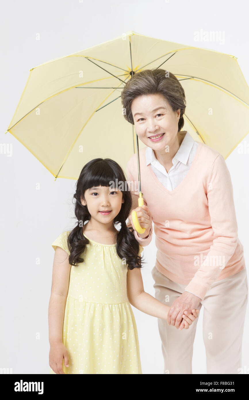 Jeune fille en robe jaune et sa grand-mère qui se tiennent la main sous le parapluie jaune les deux yeux de l'avant avec un sourire Banque D'Images