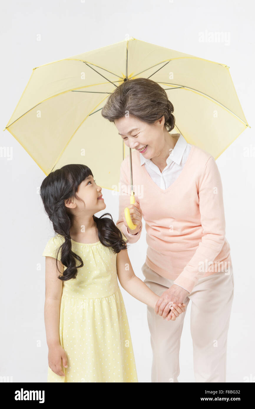 Jeune fille en robe jaune et sa grand-mère qui se tiennent la main sous le parapluie jaune à la fois les uns les autres avec des Banque D'Images