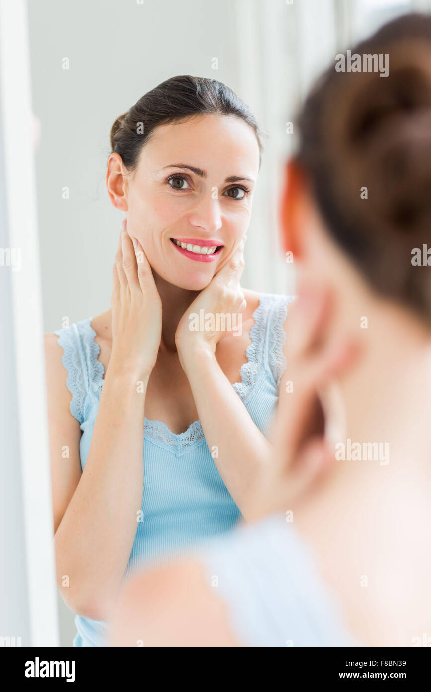 Femme contrôler son visage dans le miroir. Banque D'Images