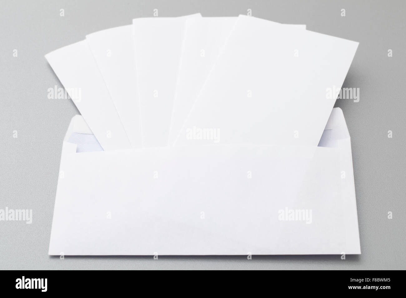 Cinq feuilles blanc plié mis en enveloppe blanche vierge, isolé sur l'arrière-plan. Banque D'Images