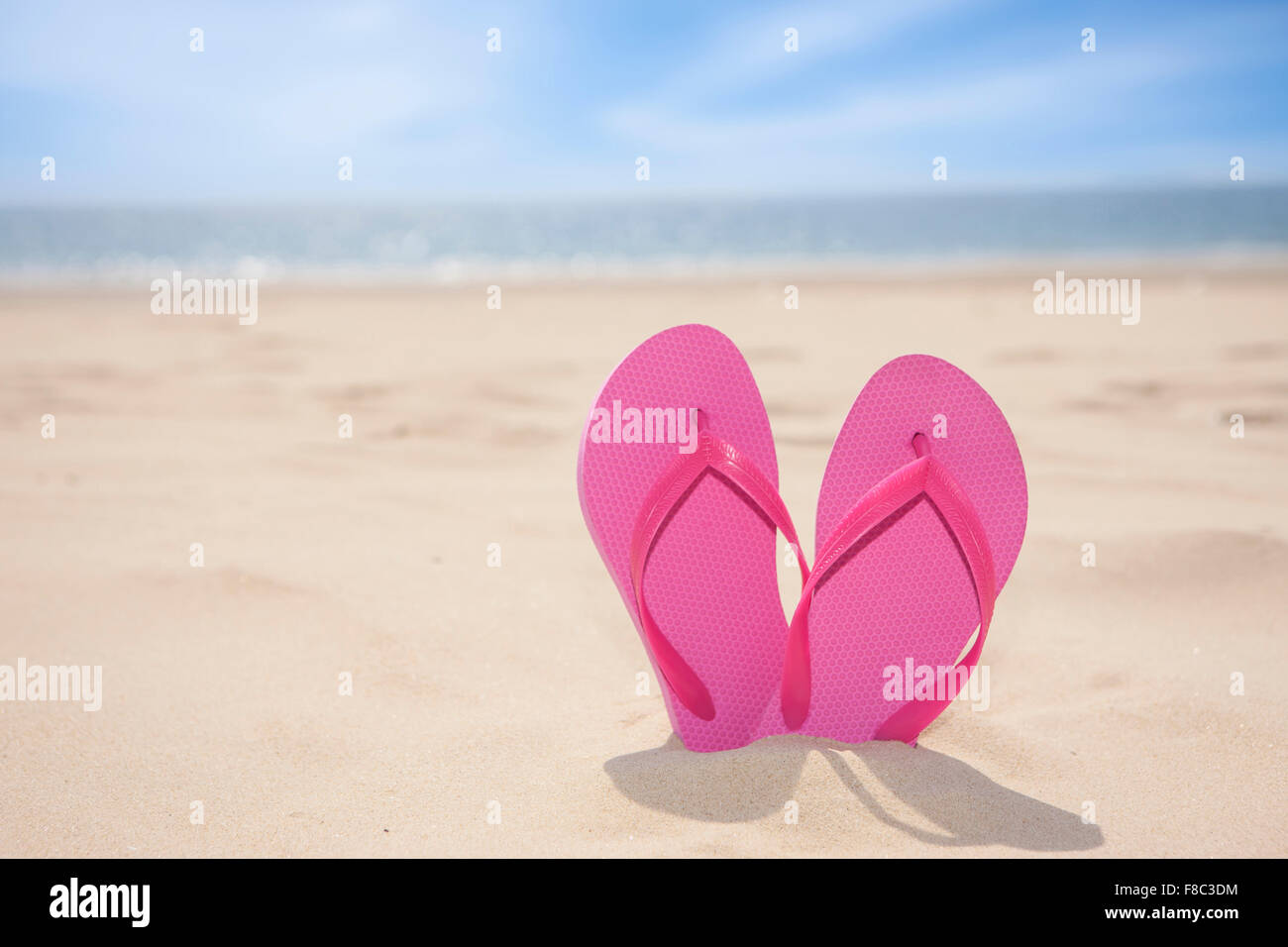 Tongs rose bloqué dans le sable n'est pas mise au point avec l'arrière-plan de plage Banque D'Images