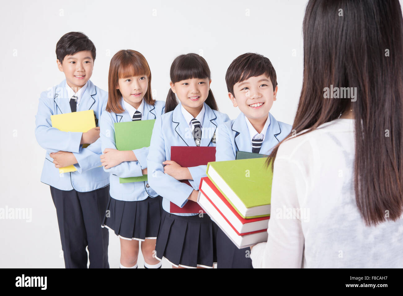 Retour apparition d'un teacher holding books et quatre élèves de l'école  élémentaire en uniforme à l'enseignant à la tenue d'un Photo Stock - Alamy