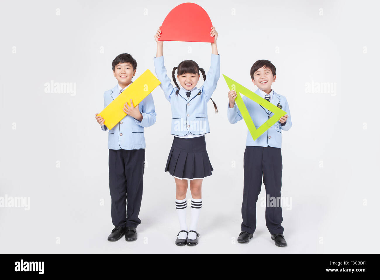 Trois garçons de l'école primaire et d'une jeune fille à l'uniforme scolaire tenant un enseignement des mathématiques et des outils avec un sourire permanent Banque D'Images