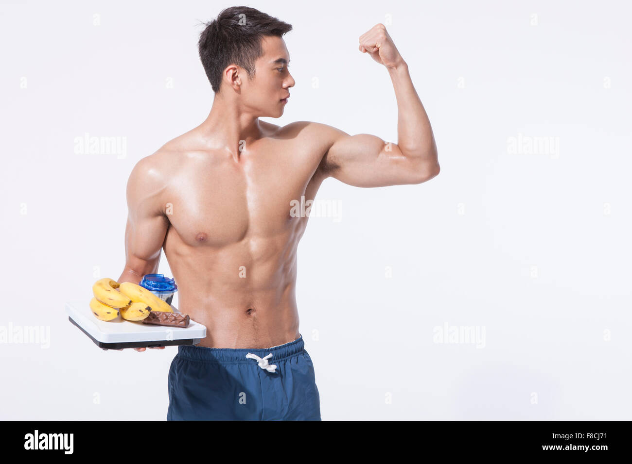L'homme musclé montrant ses biceps et tenant une échelle avec la banane et d'autres aliments et à côté Banque D'Images