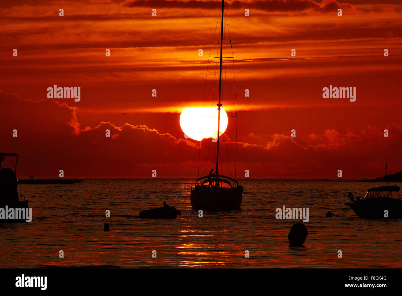 Coucher de soleil rouge mystique et paisible à un crépuscule d'été, tandis qu'un yacht arrive à port, dans la baie de Baiona, Galice, Espagne Banque D'Images