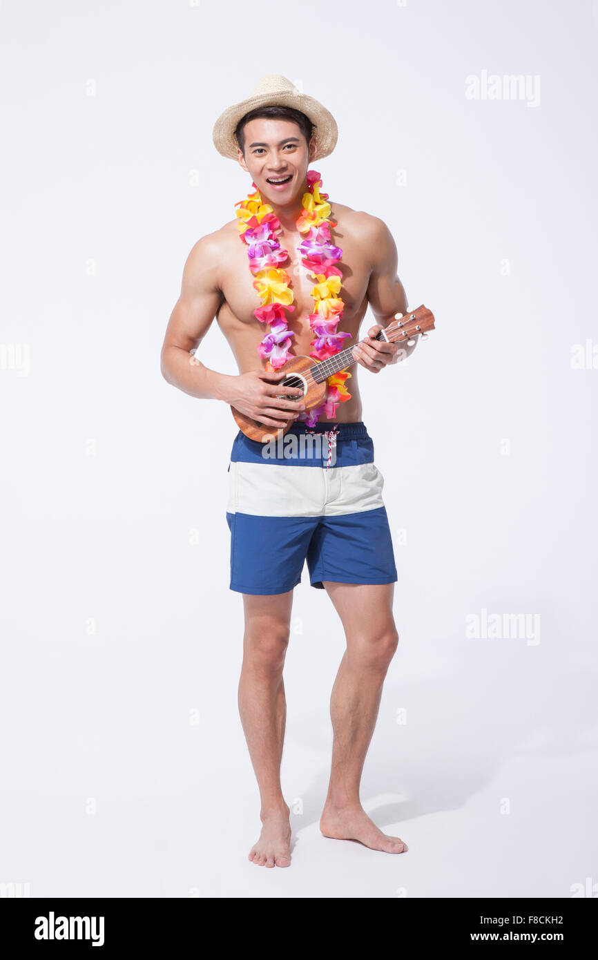 L'homme musclé en natation, pantalon, chapeau portant un collier de fleurs  debout avec un ukulele avec un sourire Photo Stock - Alamy