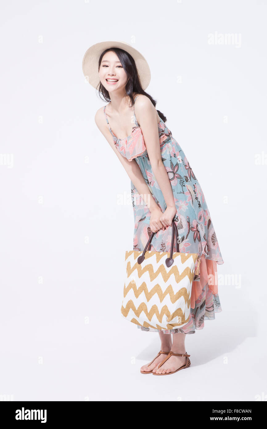 Femme aux cheveux longs en robe et un chapeau debout avec un sac dans ses mains avec son corps légèrement pliés Banque D'Images