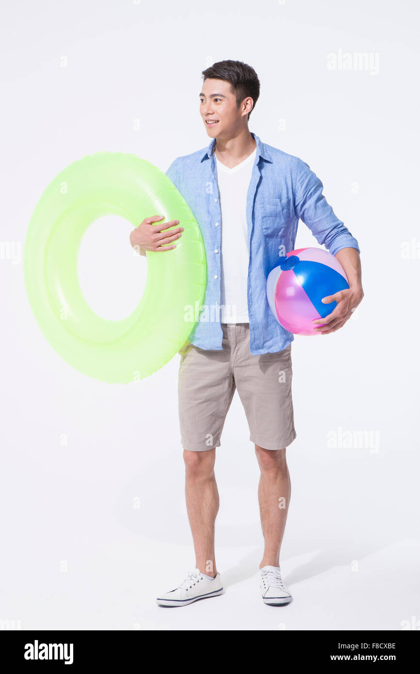Dans l'homme tenues décontractées debout et tenant un anneau tube et un ballon de plage dans chaque main Banque D'Images