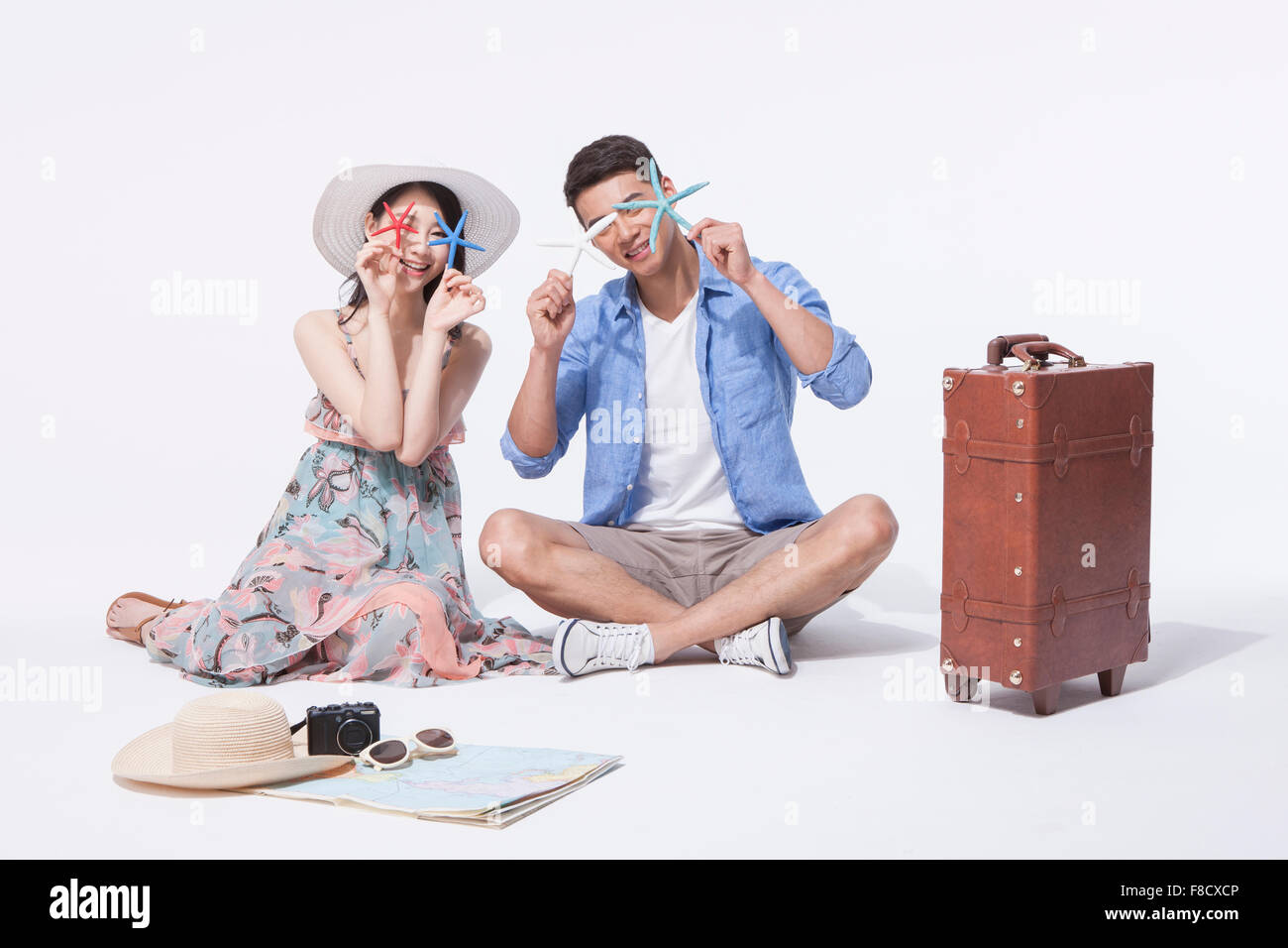 Dans l'homme tenues décontractées assis sur le plancher avec une femme en robe portefeuille et une étoile de mer pour couvrir leurs yeux avec d'autres voyages Banque D'Images