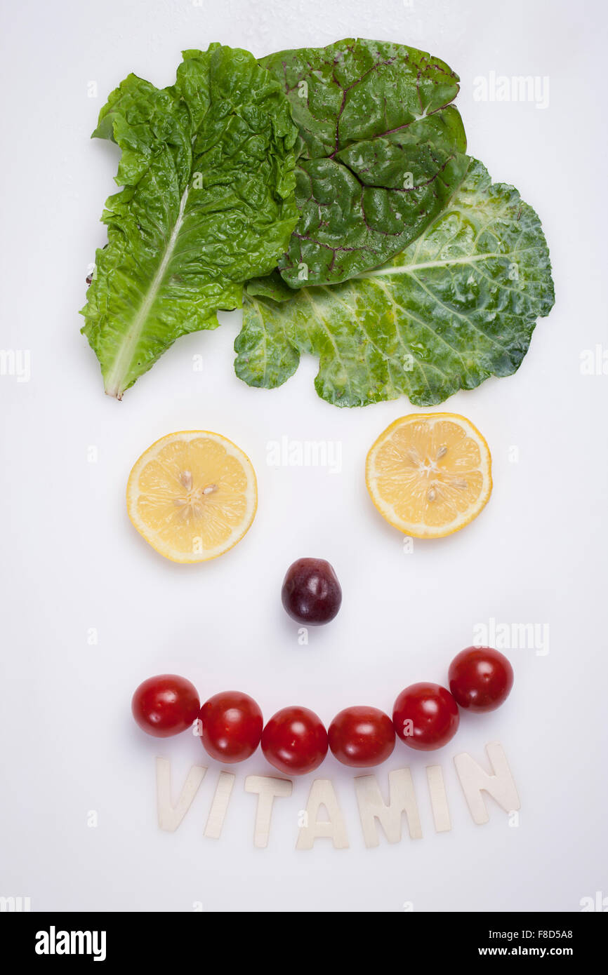 Food art faire un visage souriant faite avec la laitue, les tranches de citron, un raisin, et des tomates cerises Banque D'Images