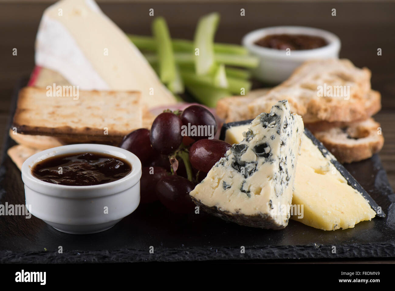 Un plateau de fromages sur ardoise avec le chutney, cheddar, stilton cheese, craquelins, brie, les raisins et le céleri. Banque D'Images