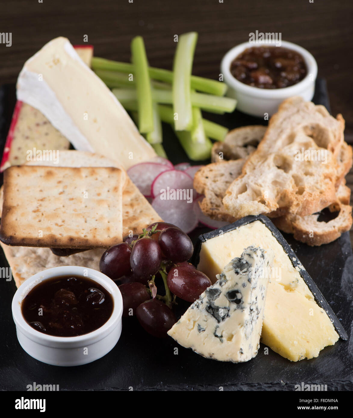 Un plateau de fromages sur ardoise avec le chutney, cheddar, stilton cheese, craquelins, brie, les raisins et le céleri. Banque D'Images