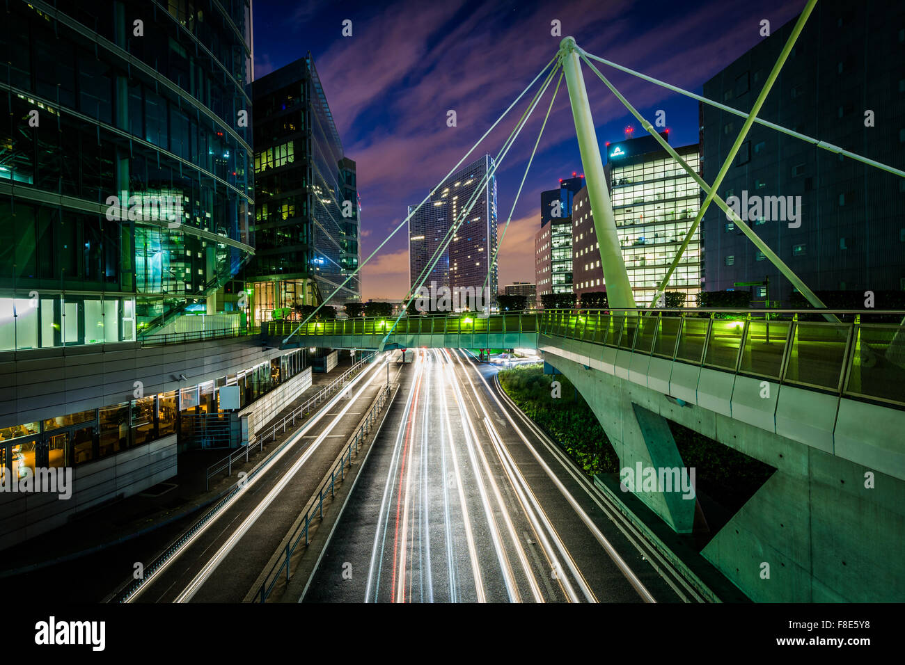 Passerelle pour piétons et les bâtiments modernes à côté d'une route de nuit à La Défense, à Paris, France. Banque D'Images