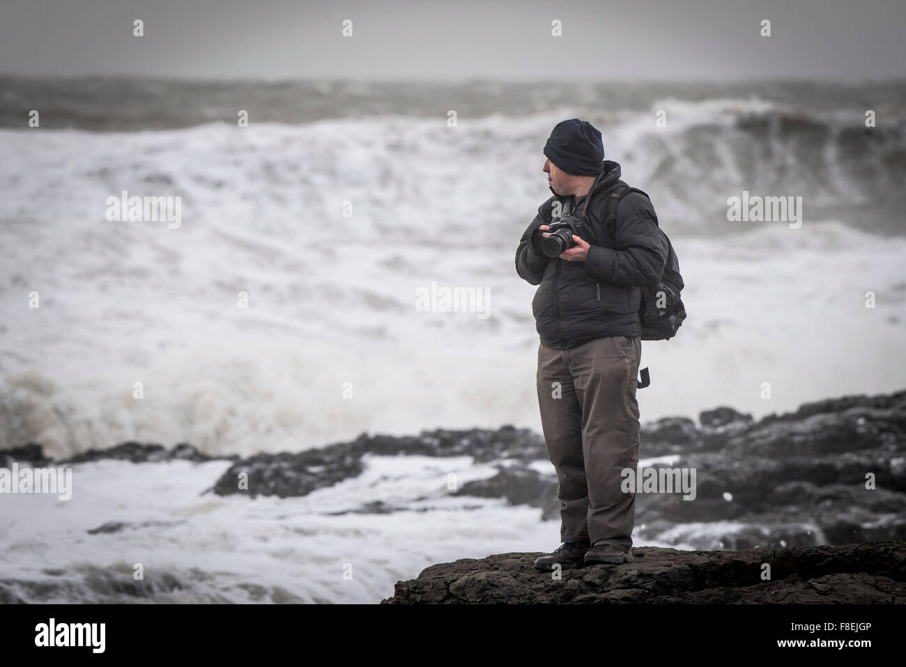 Un photographe debout sur des rochers comme une mer livre la côte à Porthcawl, Galles du Sud. Banque D'Images