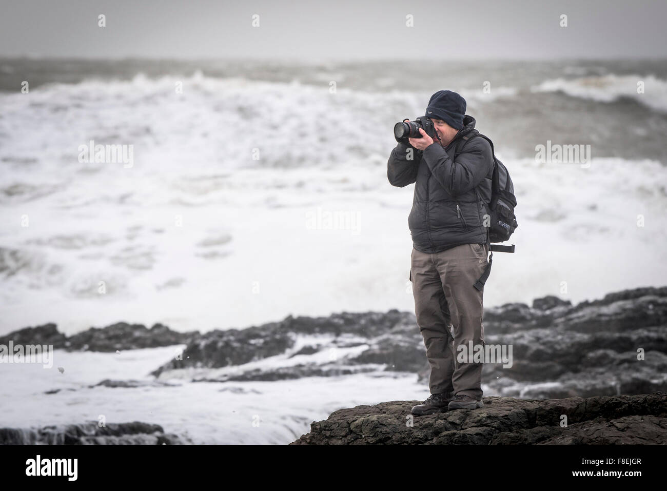Un photographe debout sur des rochers comme une mer livre la côte à Porthcawl, Galles du Sud. Banque D'Images