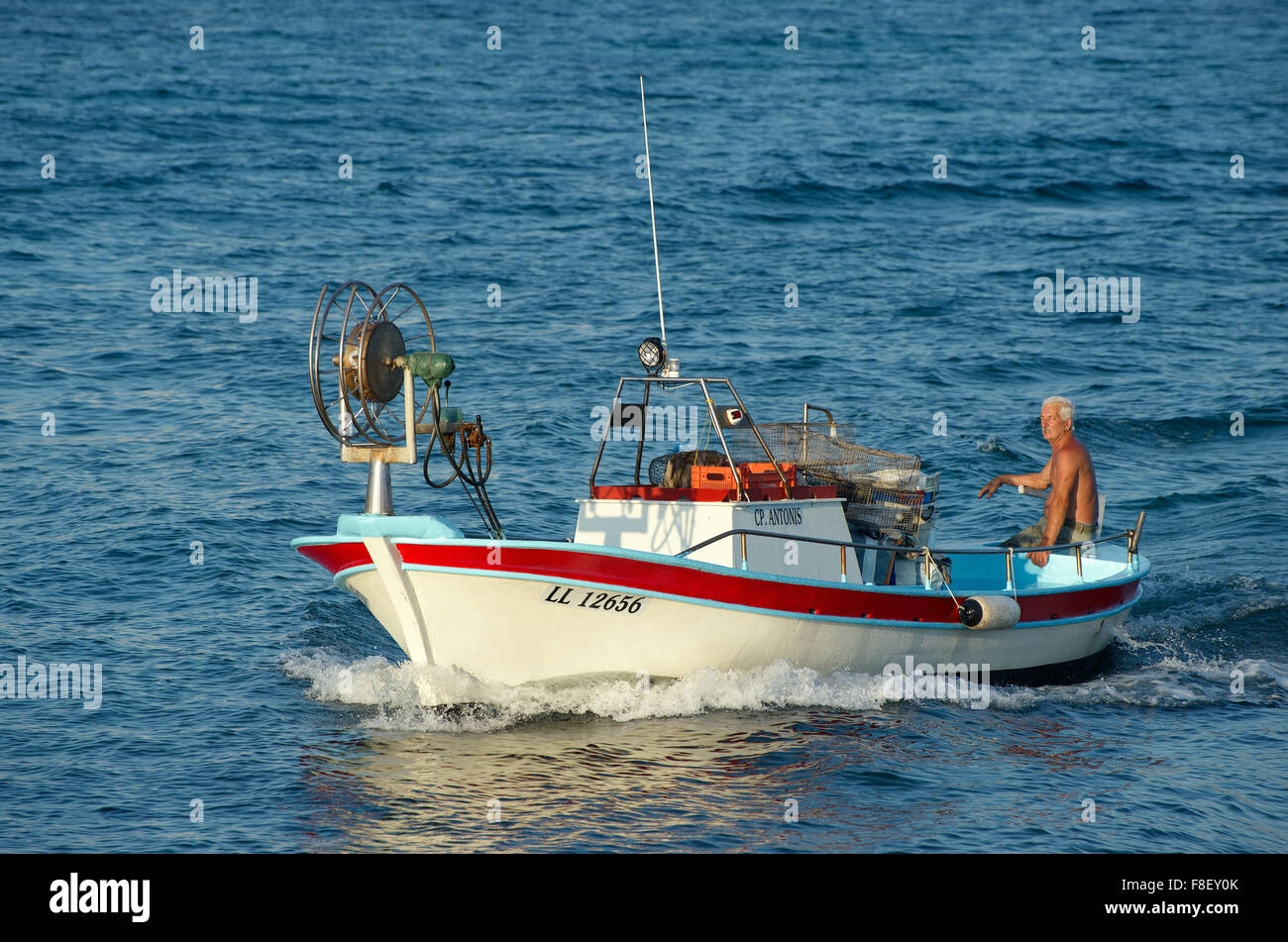 Nage pêcheur sur son bateau de pêche dans la mer dans le soleil couchant, Ayia Napa Banque D'Images