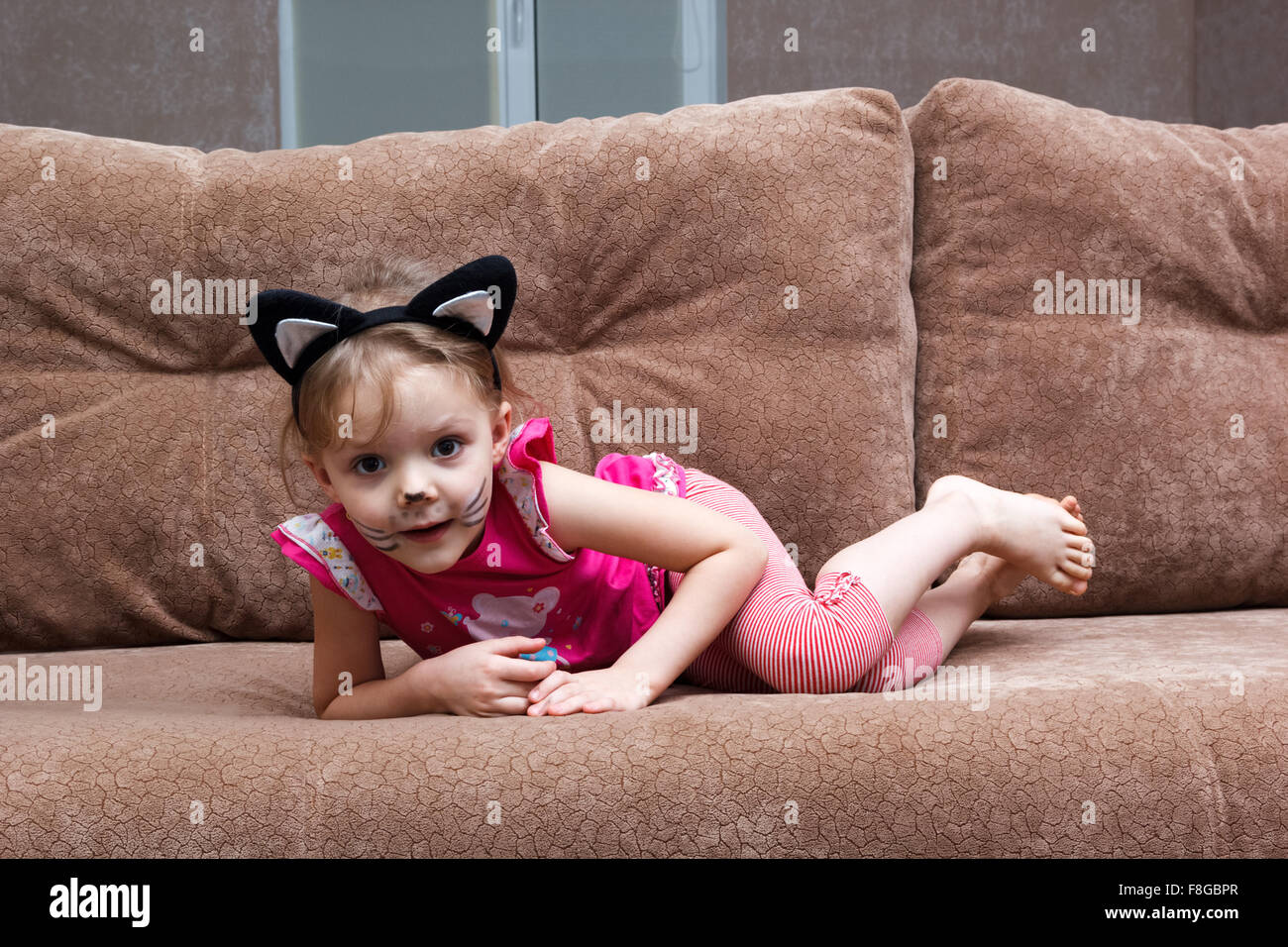 Little girl with cat face painting on a couch Banque D'Images