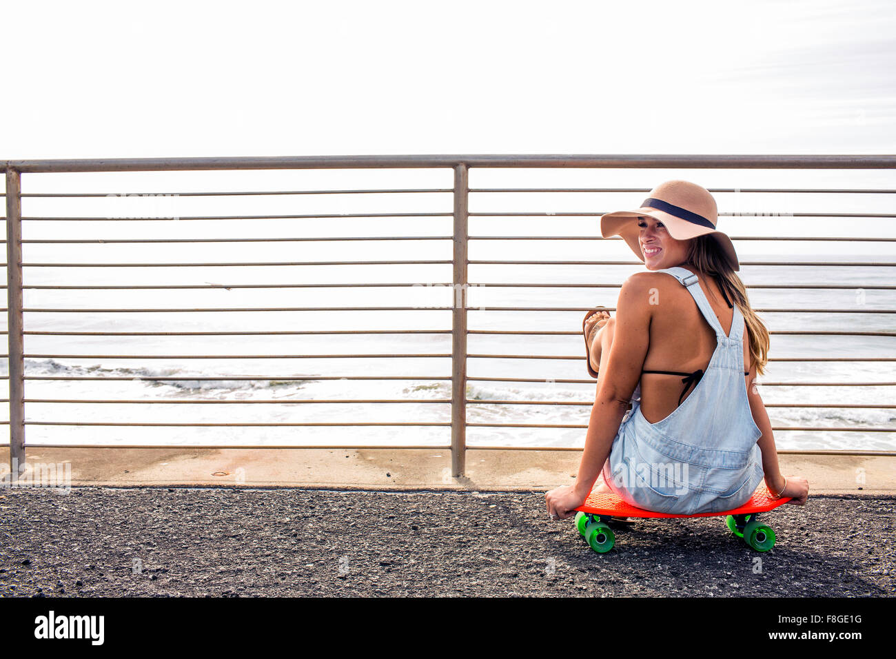 Caucasian woman sitting on skateboard at beach Banque D'Images