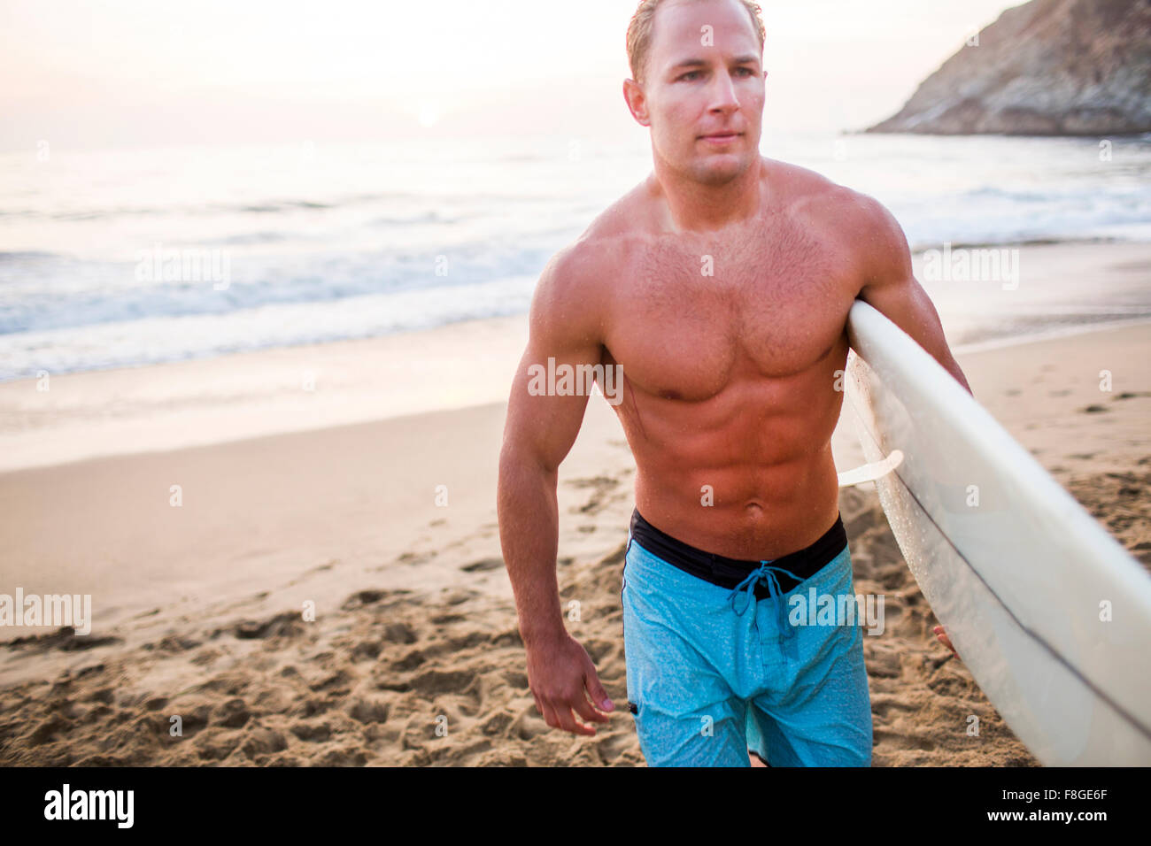 Caucasian surfer carrying surfboard on beach Banque D'Images