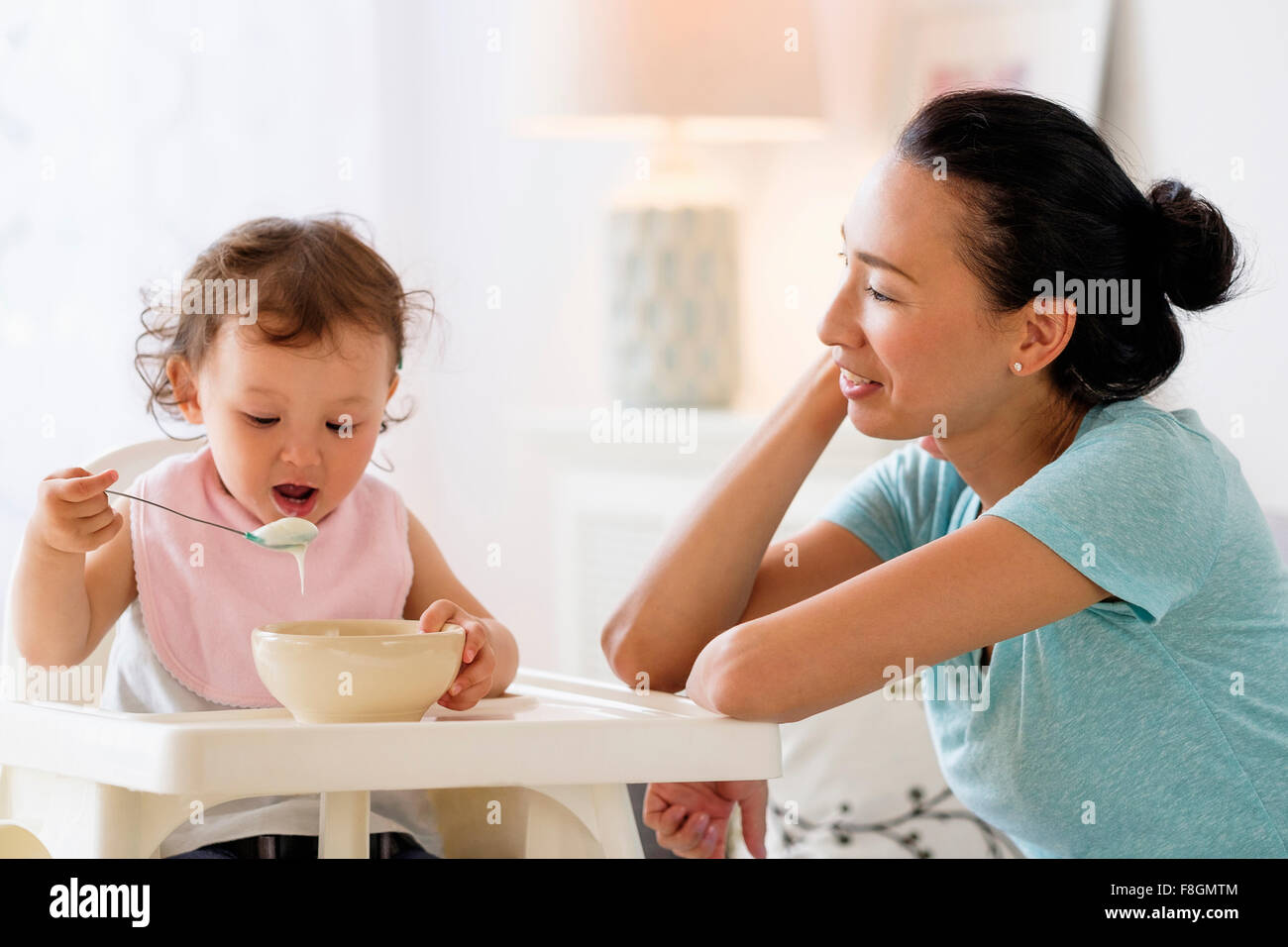 Mère regardant bébé fille manger dans une chaise haute Banque D'Images