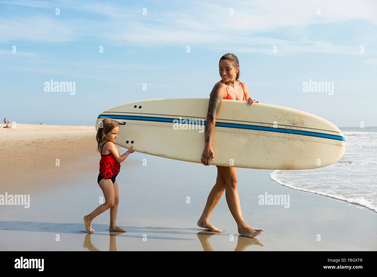 Mère et fille transportant surfboard on beach Banque D'Images