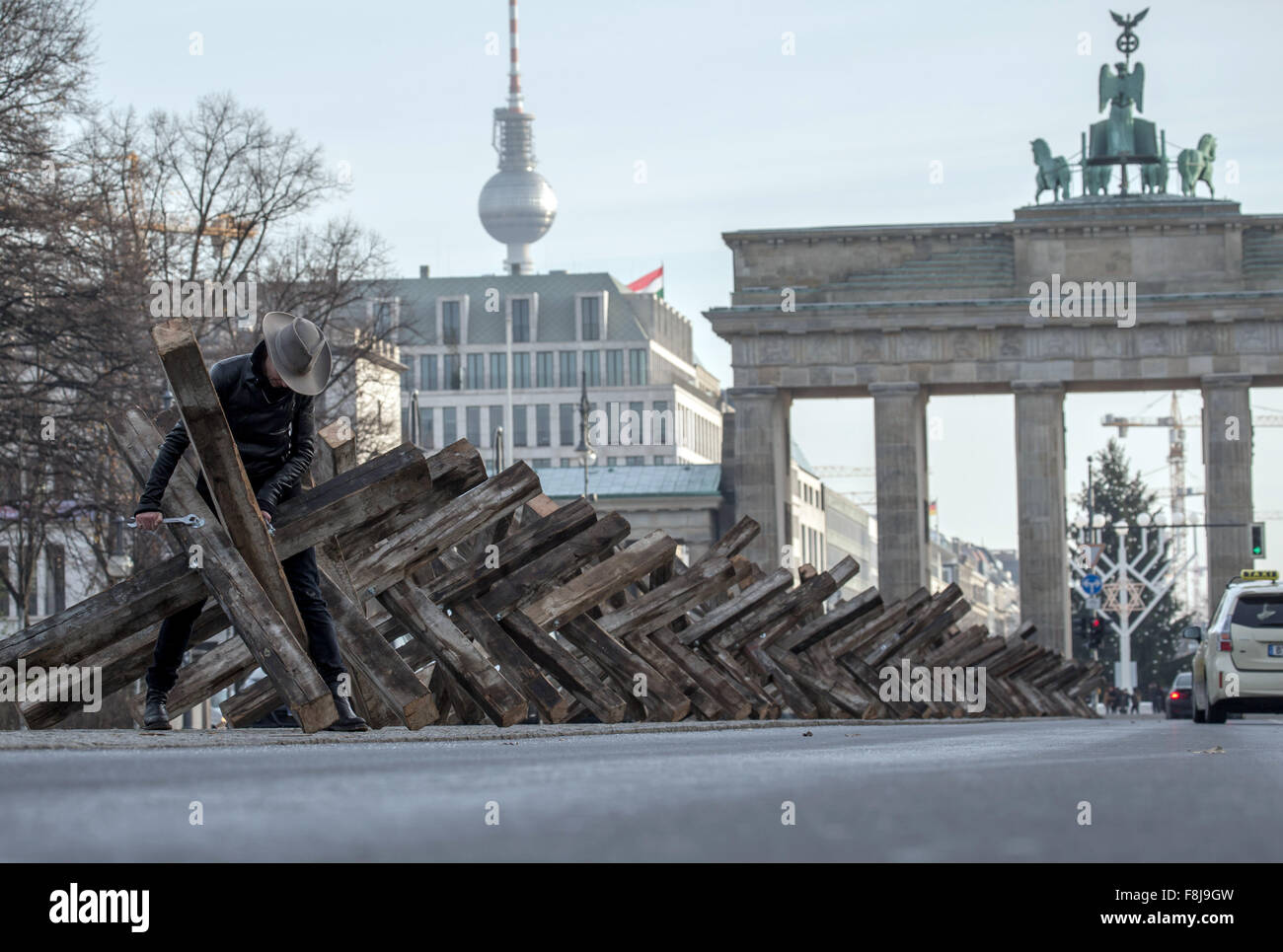 Berlin, Allemagne. Dec 10, 2015. Dafne artiste B est à son installation en bois composé de 50 obstacles antichars positionnés sur un bourrelet central d'une rue, avec la porte de Brandebourg (R) et la tour de télévision (L), représenté à l'arrière-plan, à Berlin, Allemagne, 10 décembre 2015. L'artiste a l'intention de traiter les blocs mentale à travers son art installation 'X Die Sperre im Kopf X' (lit. X La barrière dans la tête X) sur la Journée des droits de l'homme. Photo : MICHAEL KAPPELER/dpa/Alamy Live News Banque D'Images