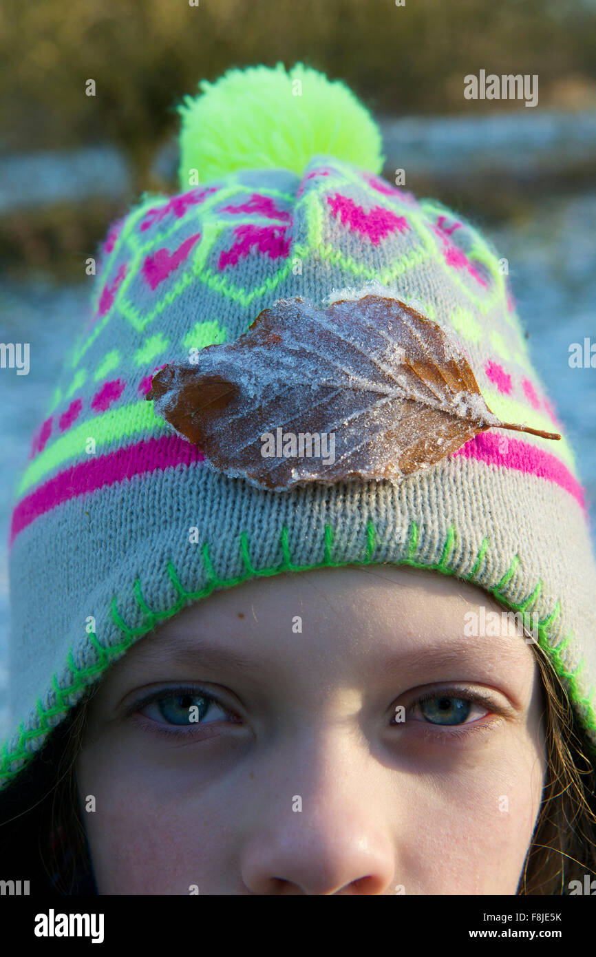 Jeune fille avec bobble hat sur avec une feuille givrée sur elle, regardant la caméra Banque D'Images