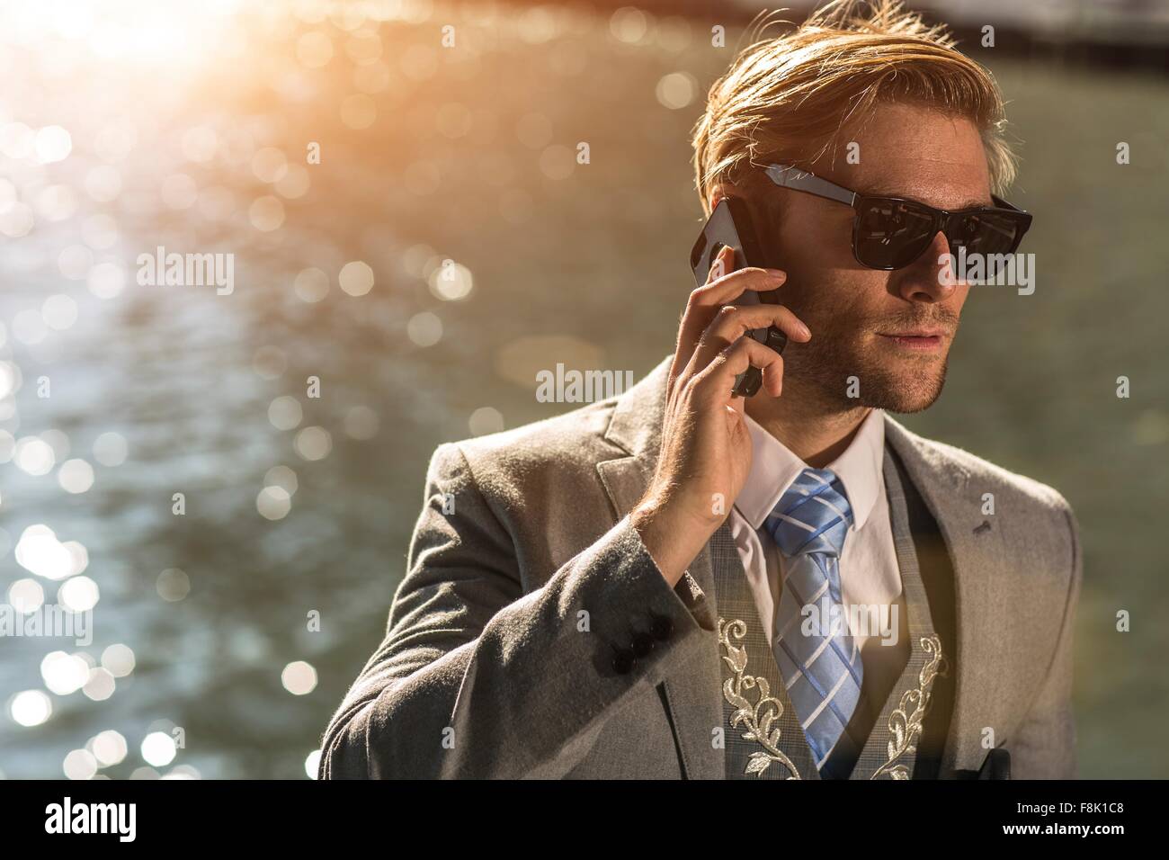 Young businessman wearing sunglasses parler sur smartphone on waterfront Banque D'Images
