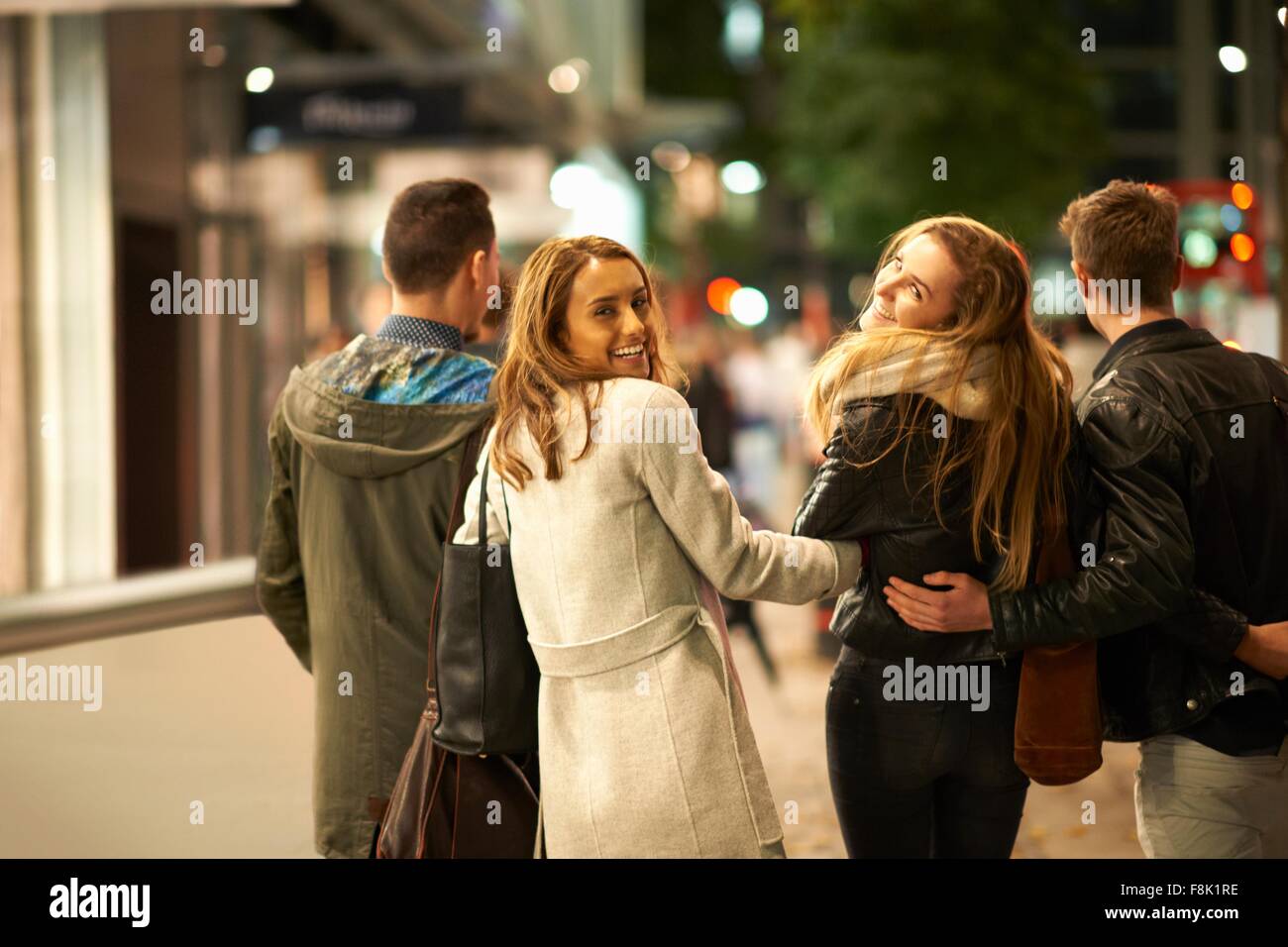 Vue arrière des deux jeunes couples se promener bras dessus bras dessous le long de rue la nuit, Londres, UK Banque D'Images
