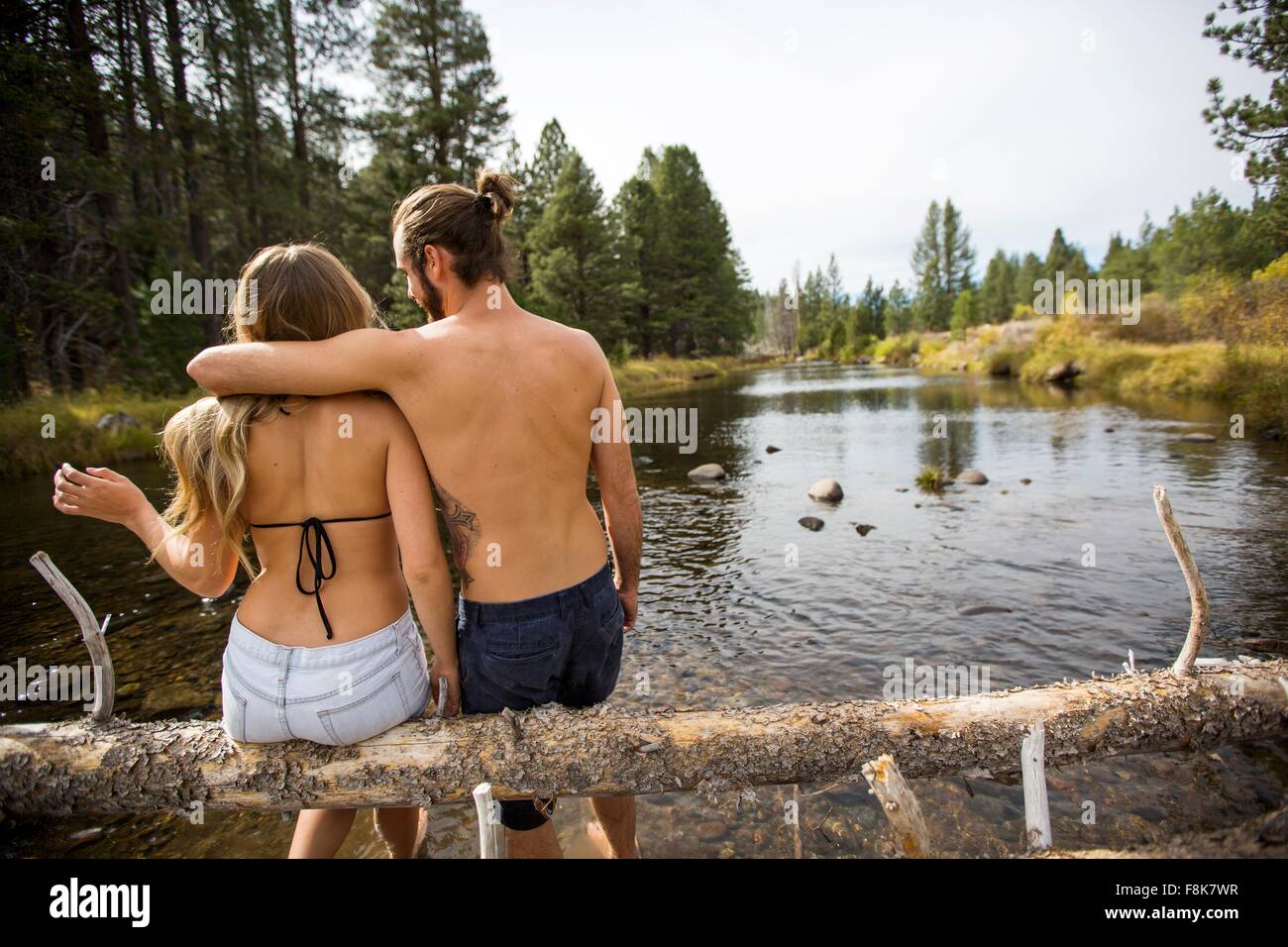 Vue arrière du jeune couple assis sur un arbre tombé dans la rivière, lac Tahoe, Nevada, USA Banque D'Images