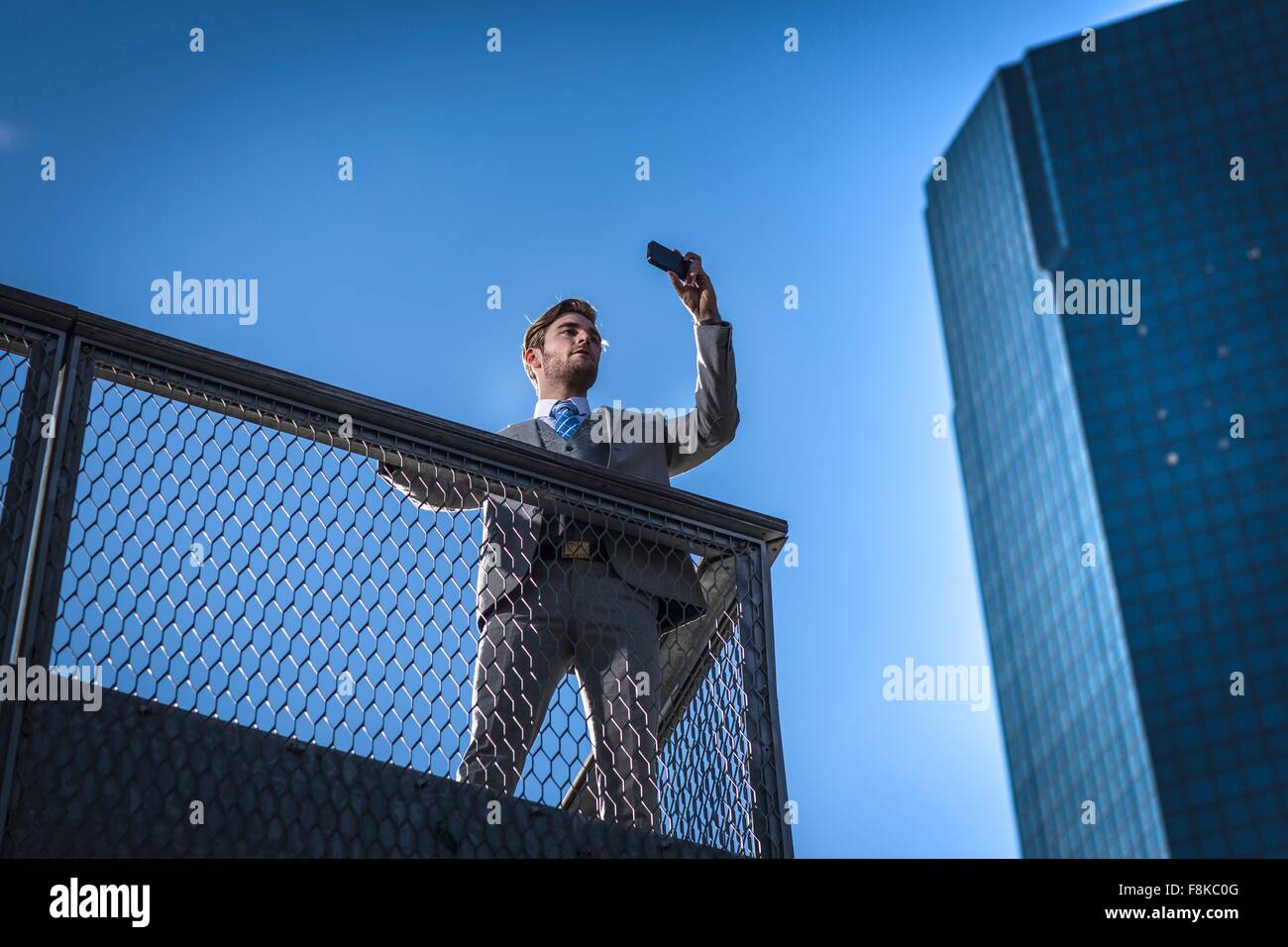 Low angle view of young businessman taking sur smartphone selfies sur balcon-ville, New York, USA Banque D'Images