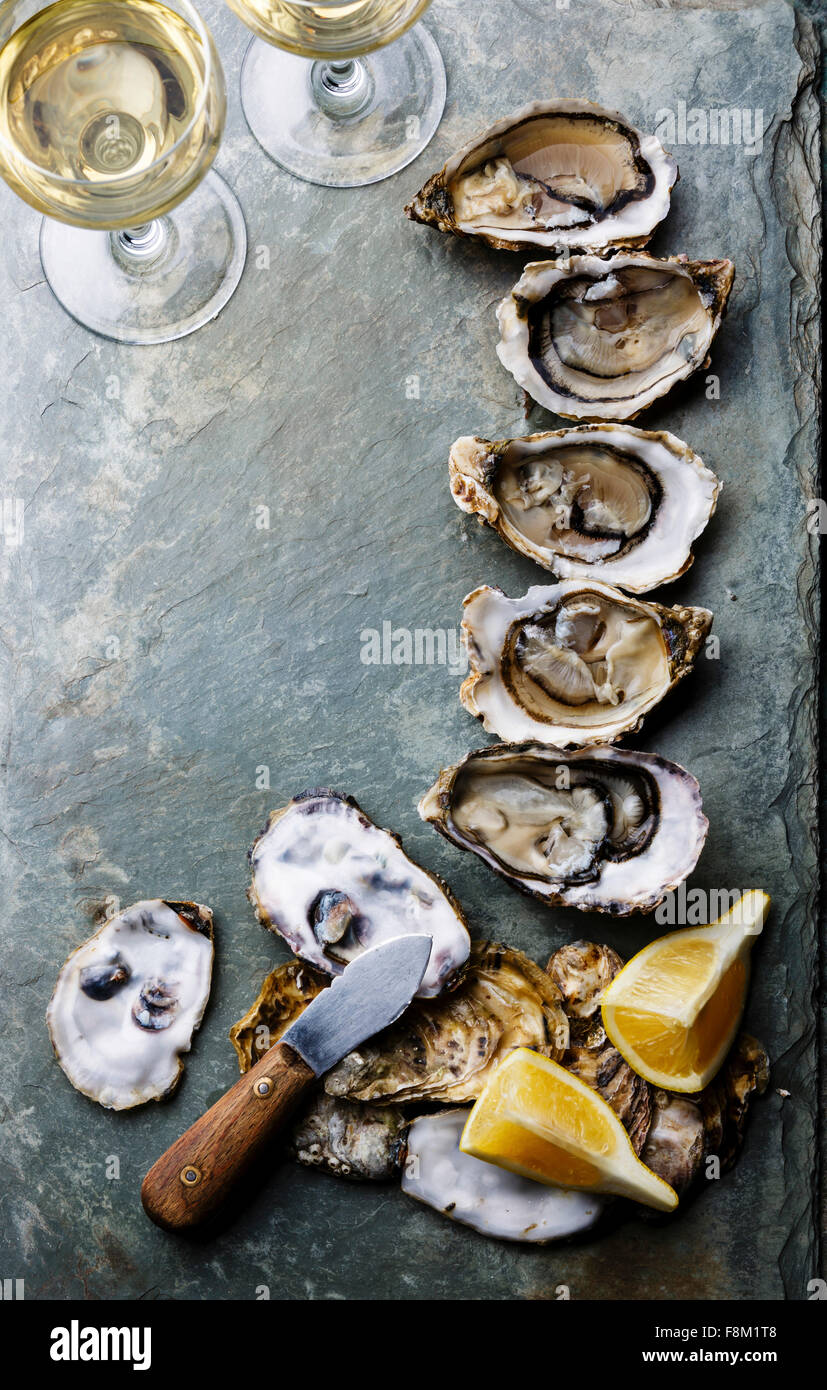 Ouvrir les Huîtres Fines de claire sur fond de plaque en pierre avec le citron et le vin blanc Banque D'Images Ouvrir les Huîtres Fines de claire sur fond de plaque en pierre avec le citron et le vin blanc Banque D'Images