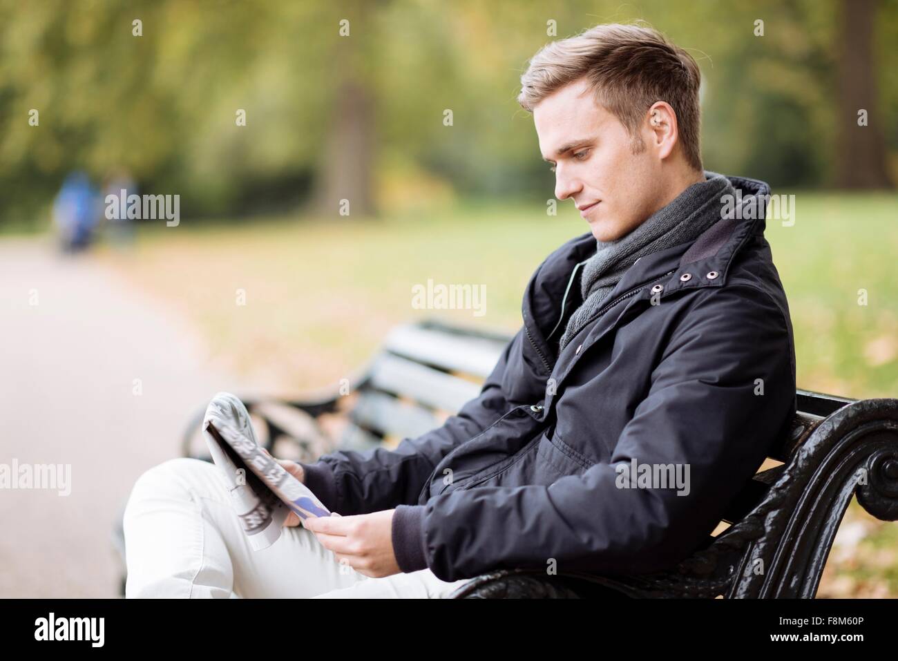 Young man sitting on bench reading newspaper in park Banque D'Images
