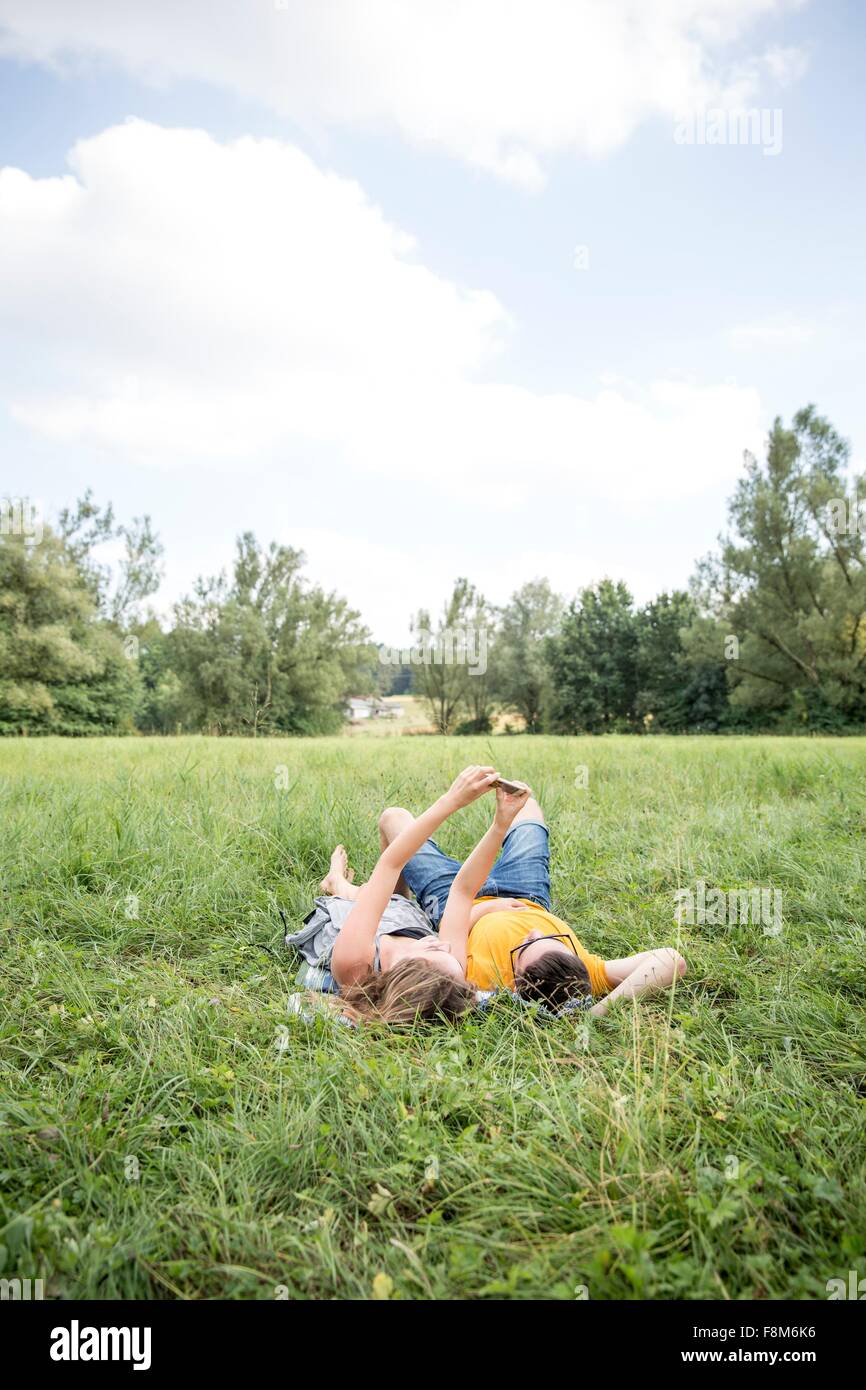 Jeune couple lying in field, taking self portrait using smartphone Banque D'Images