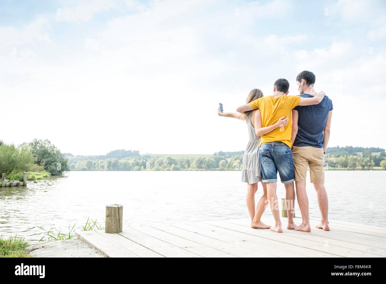 Trois jeunes adultes standing on Jetty, taking self portrait, à l'aide de smartphone, vue arrière Banque D'Images