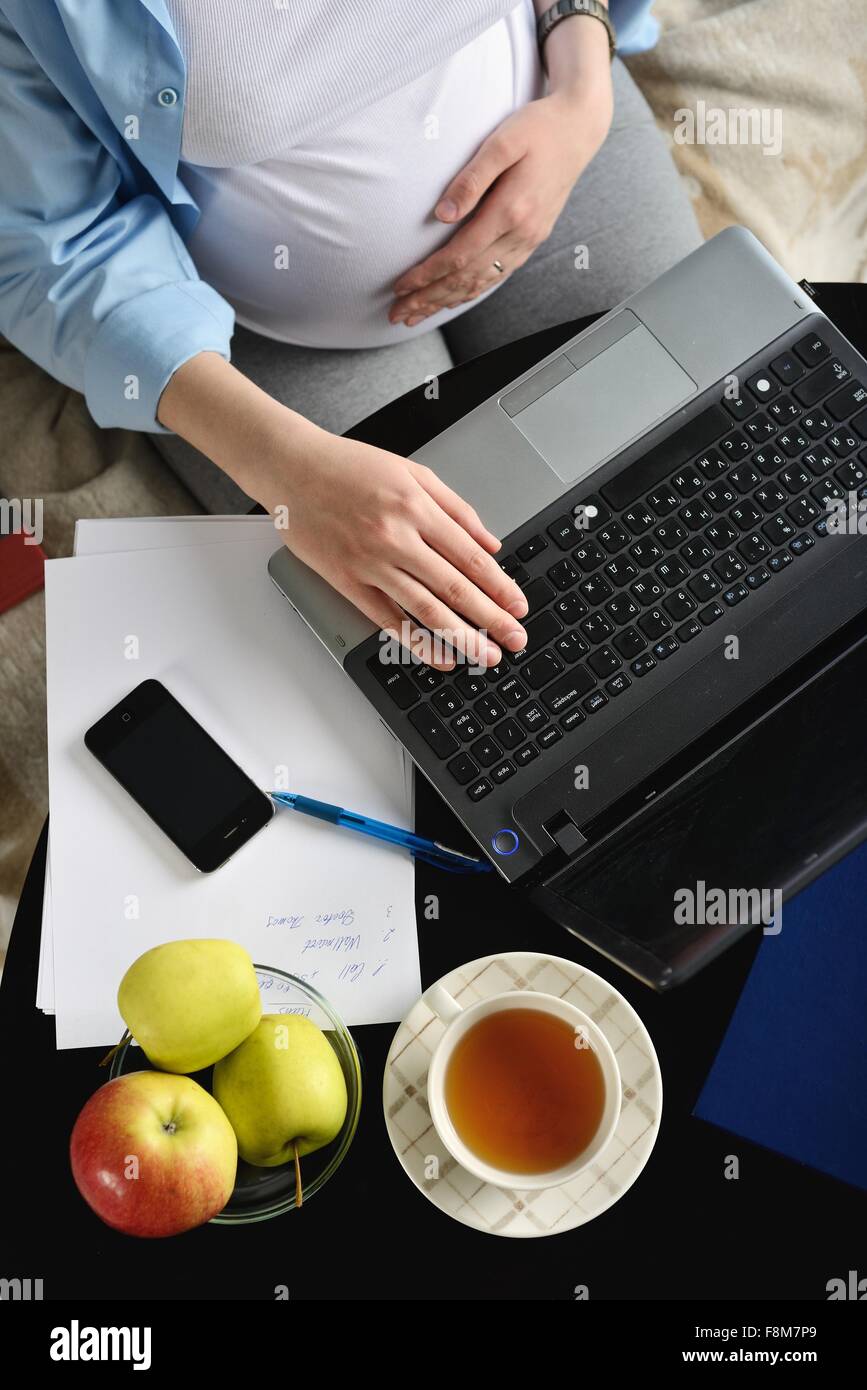 Pregnant woman sitting on sofa, using laptop, overhead view Banque D'Images