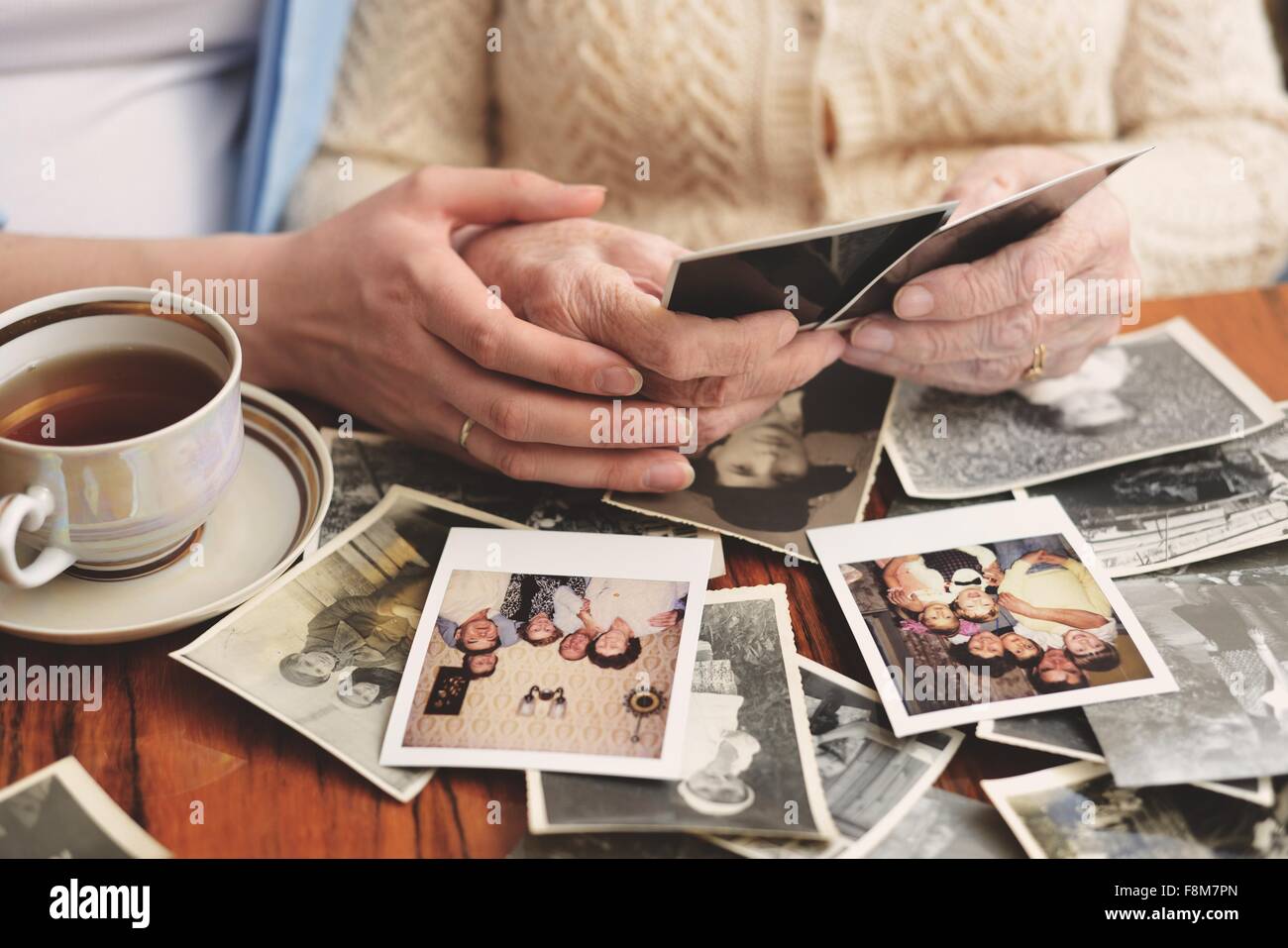 Senior woman et petite-fille assis à table, à l'intermédiaire d'anciennes photographies, mid section Banque D'Images