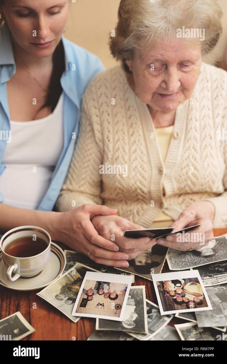 Senior woman and granddaughter sitting at table, regardant à travers des photographies anciennes Banque D'Images