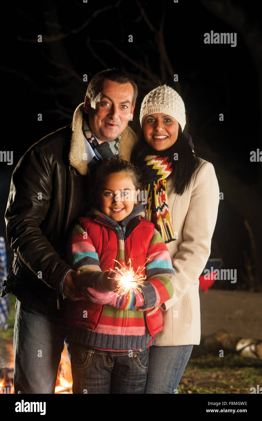 Jeune fille posant avec un sparkler sur Bonfire Night, avec ses parents Banque D'Images