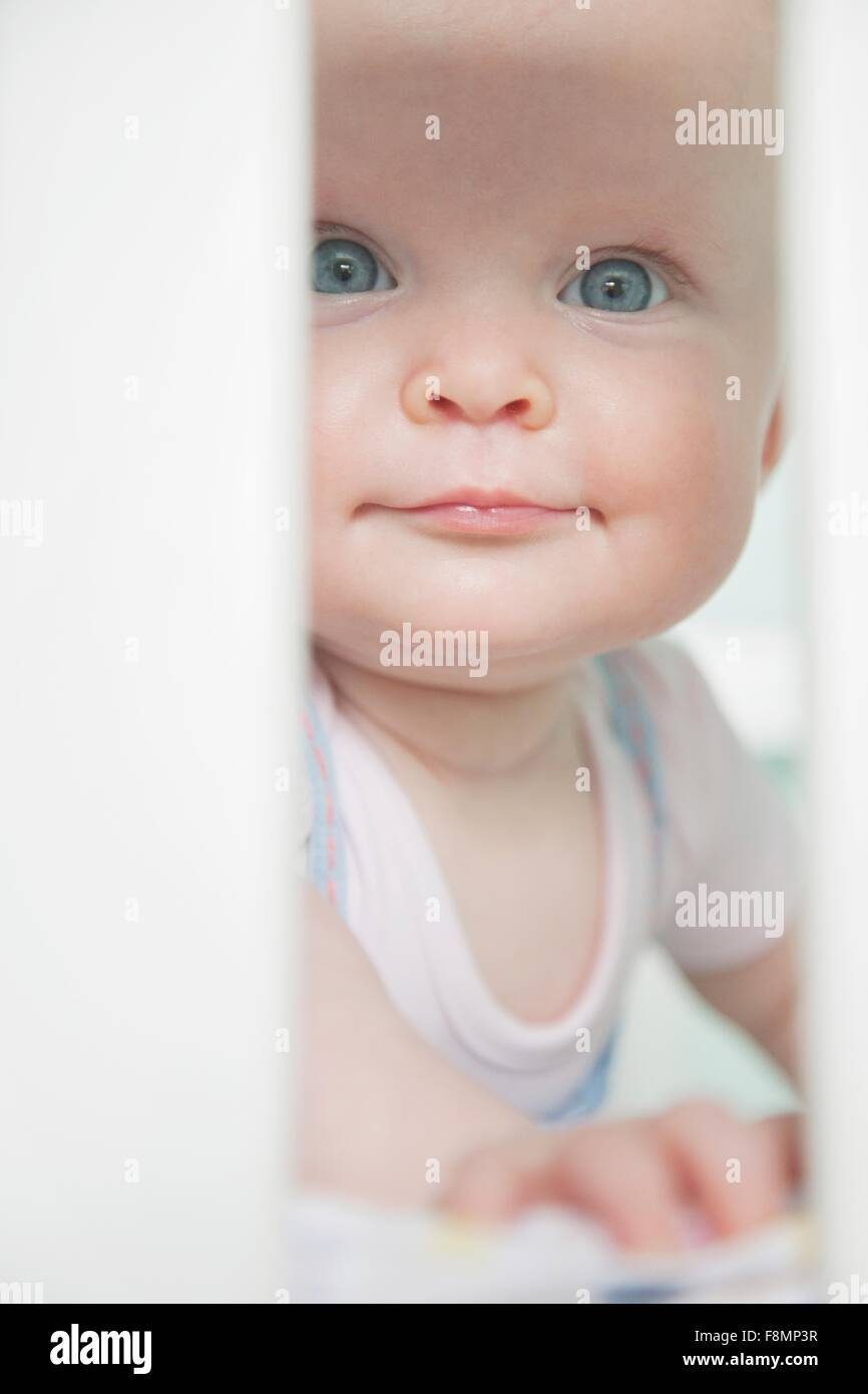 Portrait of baby girl looking through bars sur lit bébé Banque D'Images