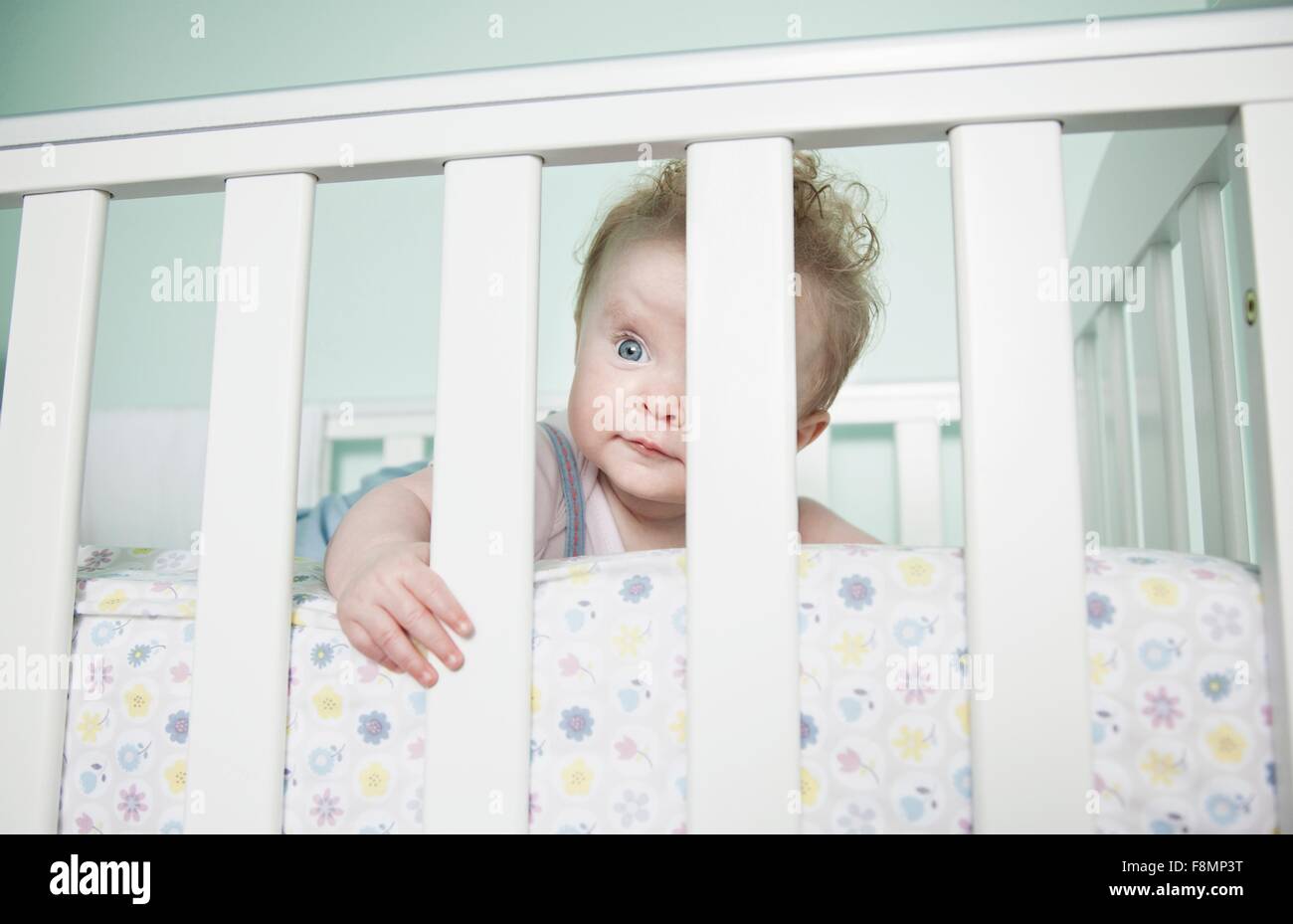 Portrait of baby girl looking through bars sur lit bébé Banque D'Images