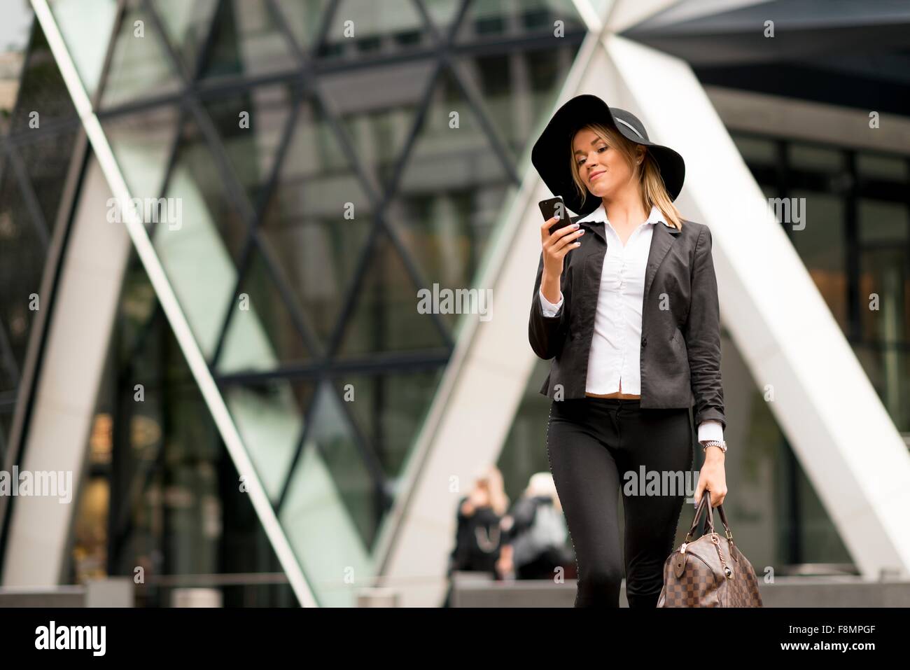 Femme textos en marchant, 30 St Mary Axe en arrière-plan, London, UK Banque D'Images