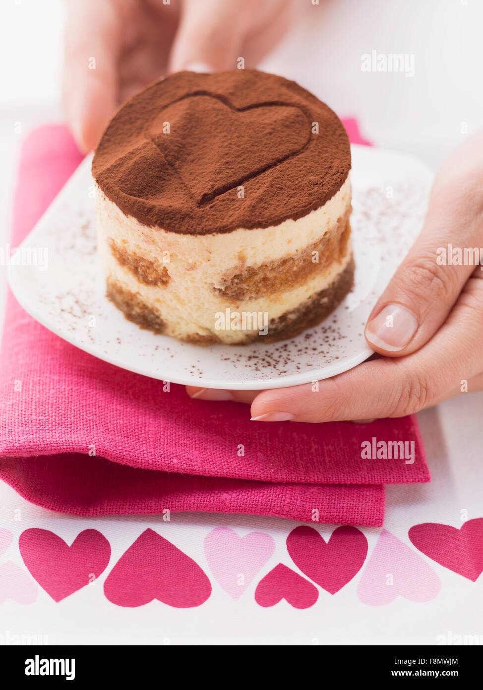 Mains au service d'une personne tiramisu avec un cœur dessiné dans la poudre de cacao sur le dessus Banque D'Images