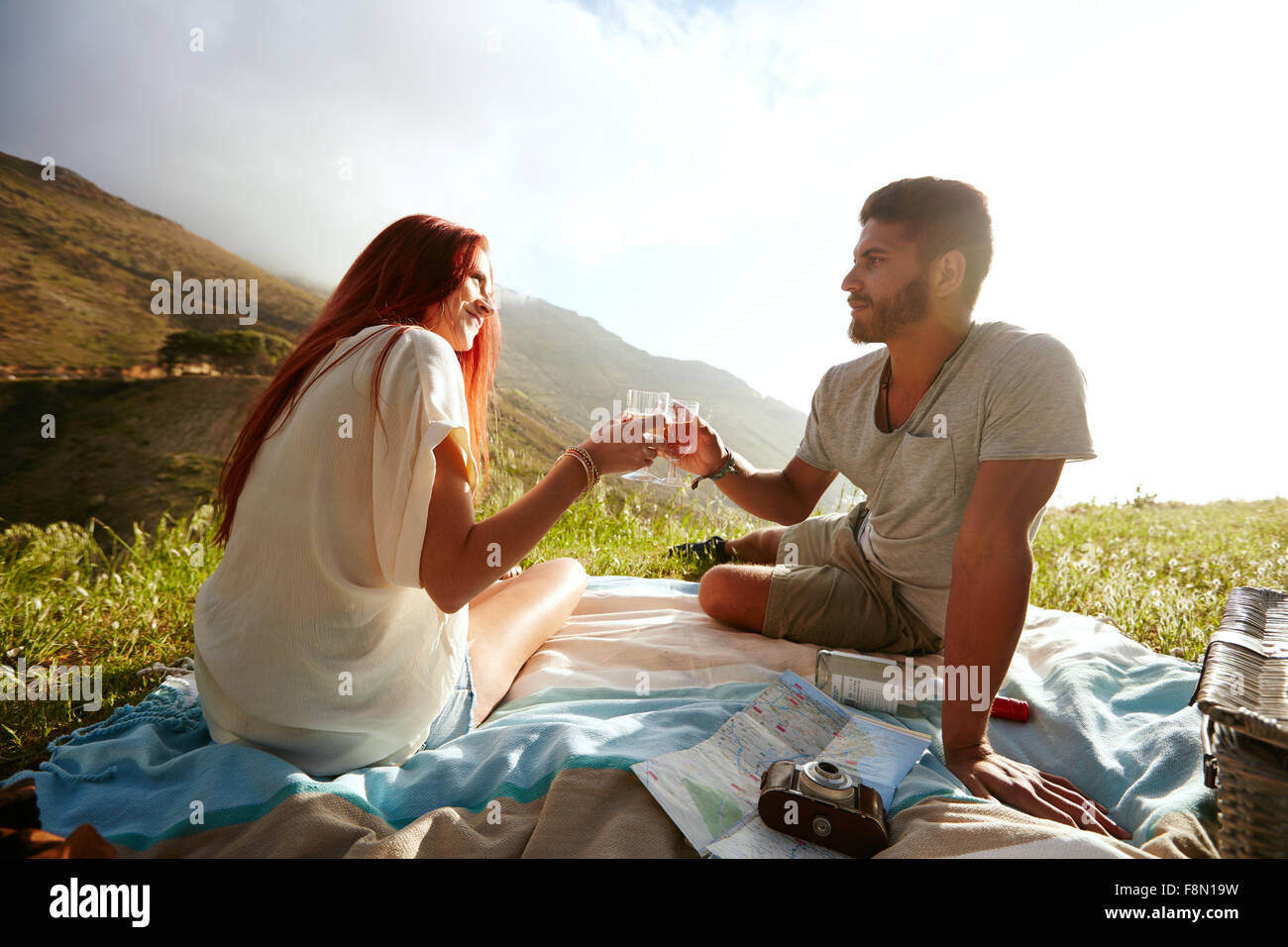 Love couple assis sur l'herbe et boire du vin au cours d'un pique-nique. Man and woman on des vacances d'été. Couple having a r Banque D'Images
