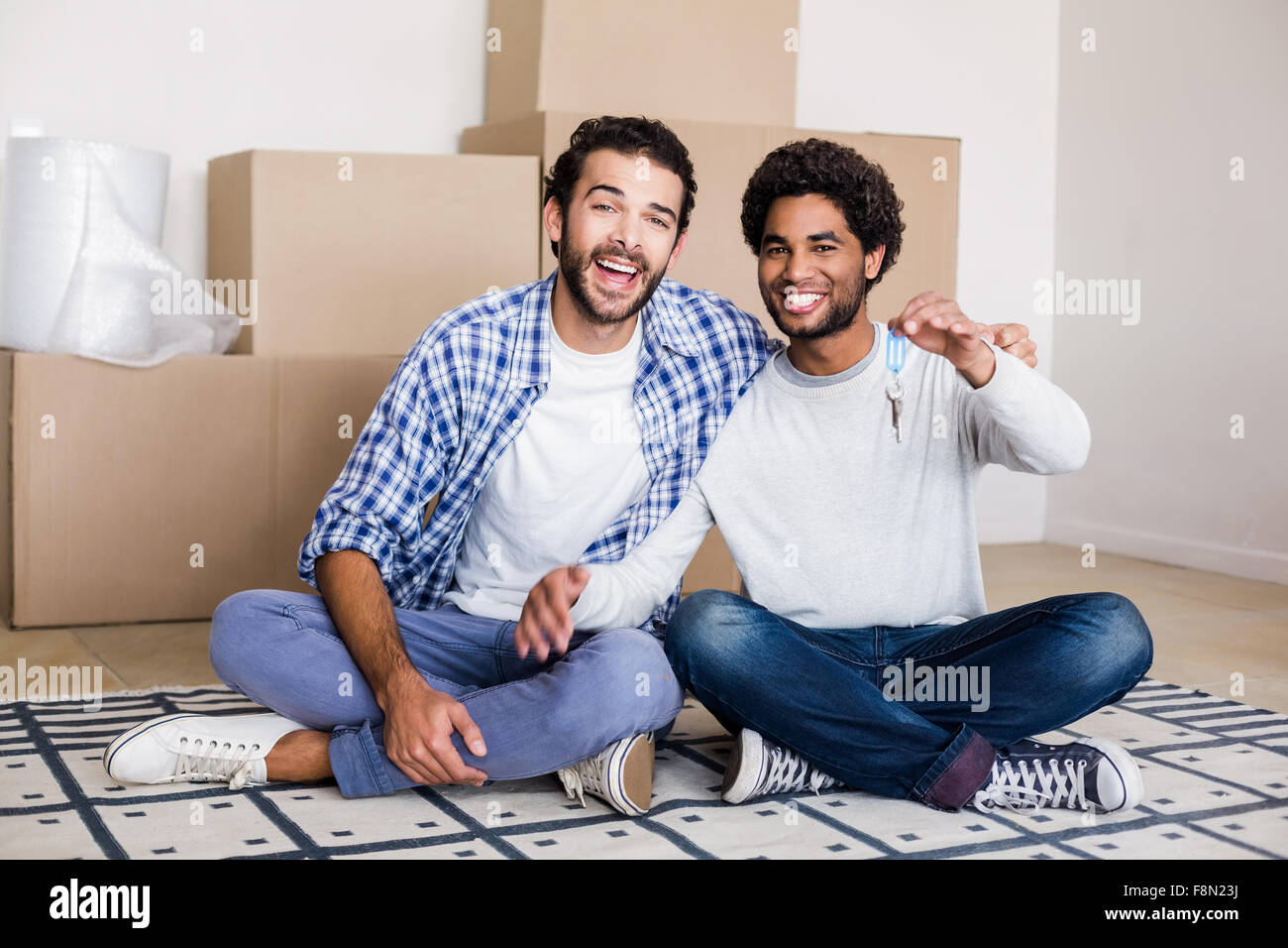 Happy gay couple holding nouvelles clés de maison sitting on floor Banque D'Images