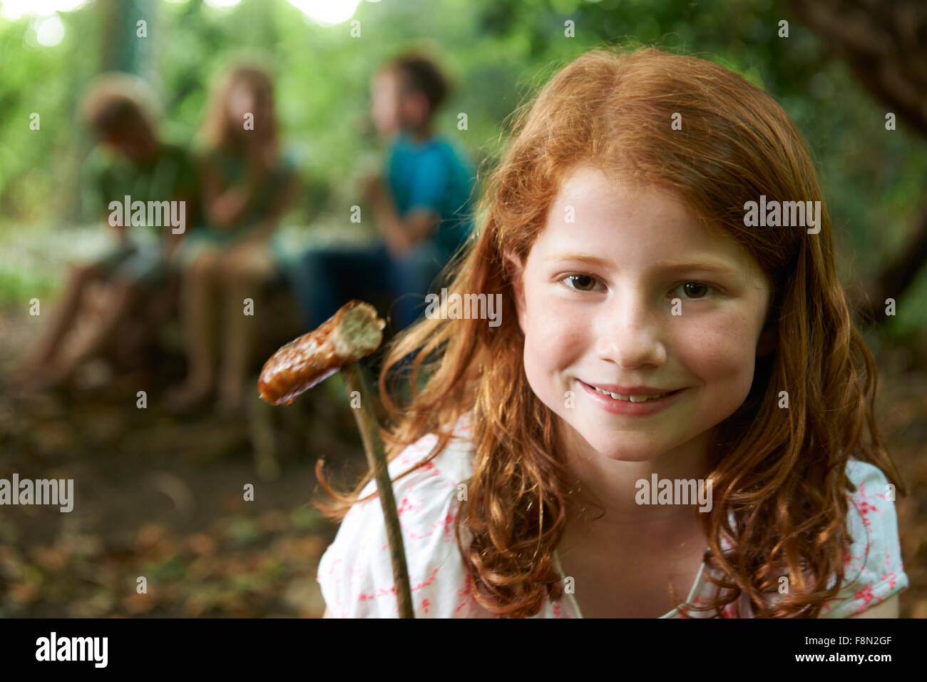Girl Eating Sausage cuits sur un feu de camp avec des amis Banque D'Images