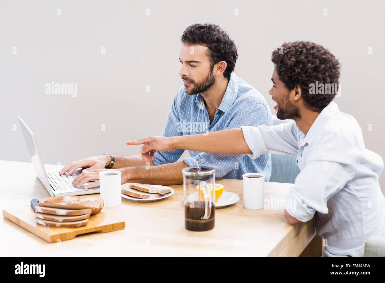 Happy gay couple having breakfast and using laptop Banque D'Images